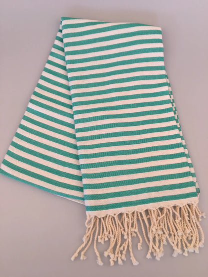 Turquoise and white striped Turkish towel with fringe edges, folded at an angle on a light background.