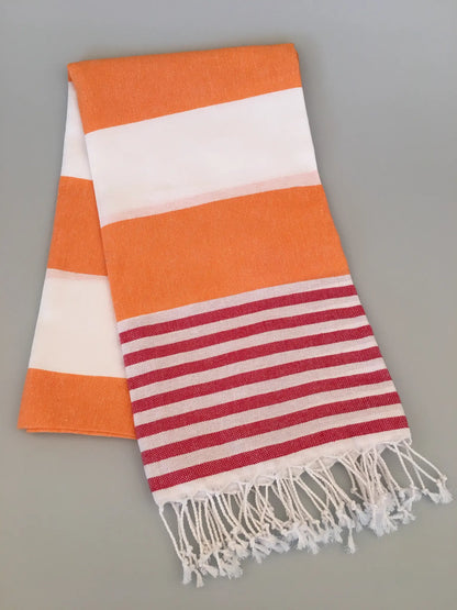 "Tralles Turkish towel peshtemal featuring orange and white stripes with red and white striped ends, fringed edges."