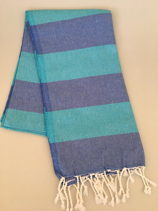 Turquoise and blue striped Turkish towel with fringed edges, laid flat on a light background.