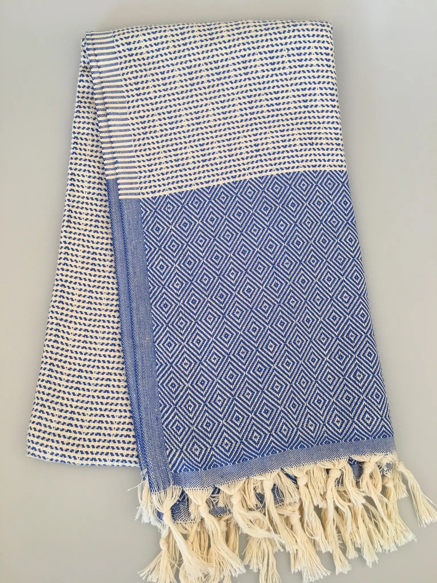"Lycia Patara Turkish towel in blue and white with diamond patterns and fringed edges, laid flat on a light surface."