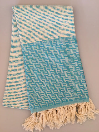 Light blue Turkish towel with diamond pattern, cream border, and fringed edges, folded on a neutral background.
