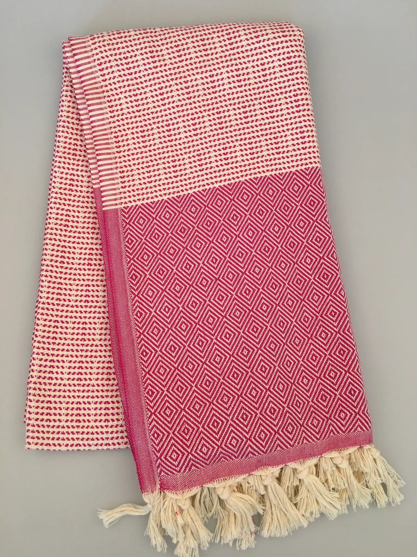 "Lycia Patara Turkish towel in pink and white, featuring diamond patterns and fringed edges, folded on a light background."