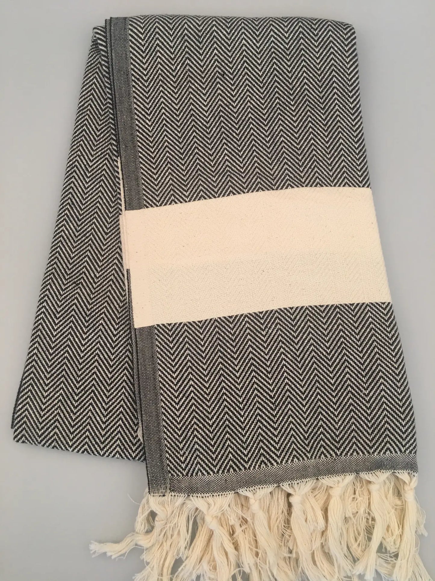 Black and white herringbone-patterned Turkish towel with a cream-colored band and fringed edges, laid flat.