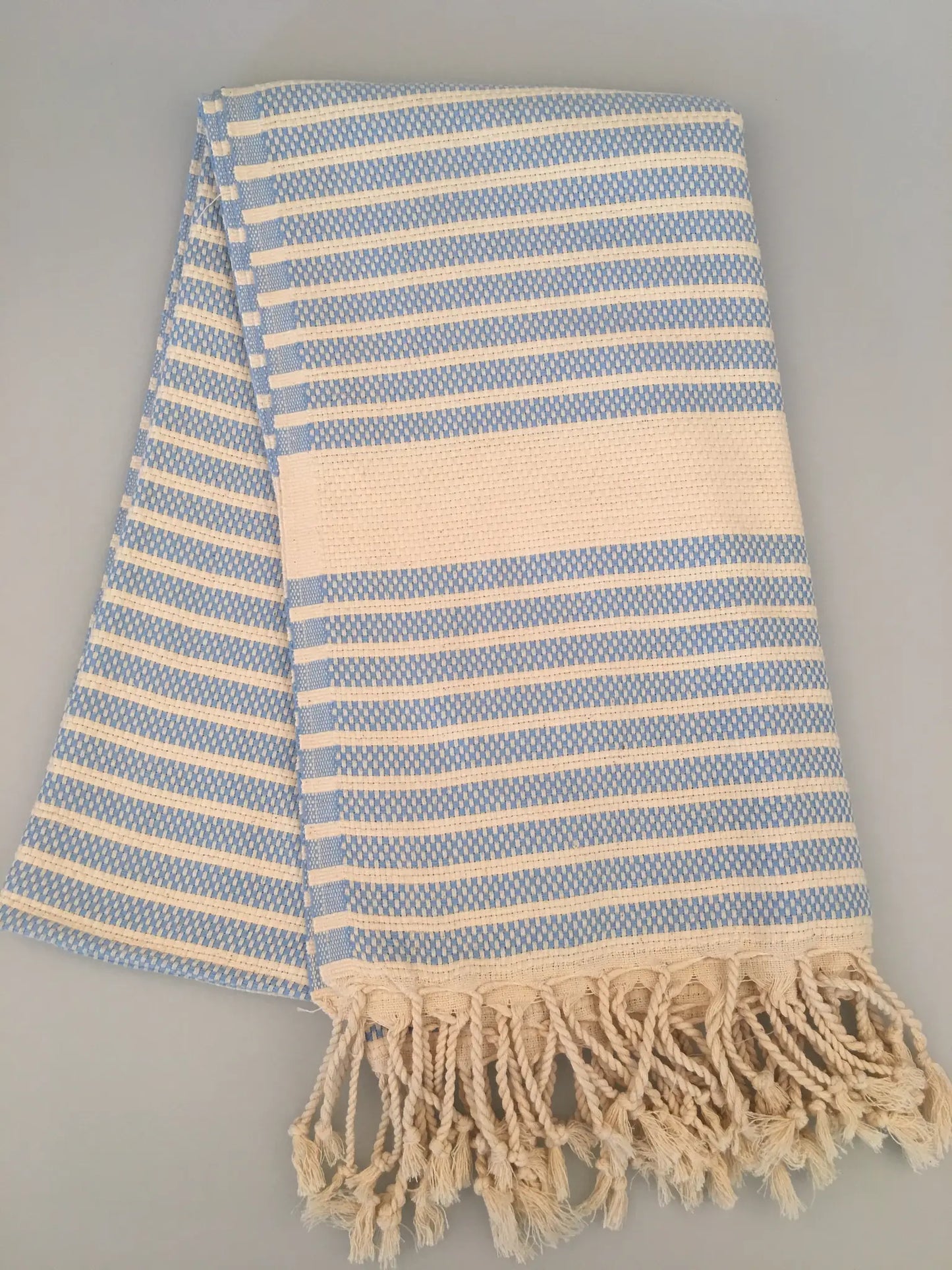Light blue and cream striped Turkish towel with fringed edges, folded on a neutral background.