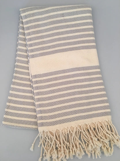 Hittite Turkish towel in gray and cream with striped pattern and fringed edges, laid flat on a gray background.