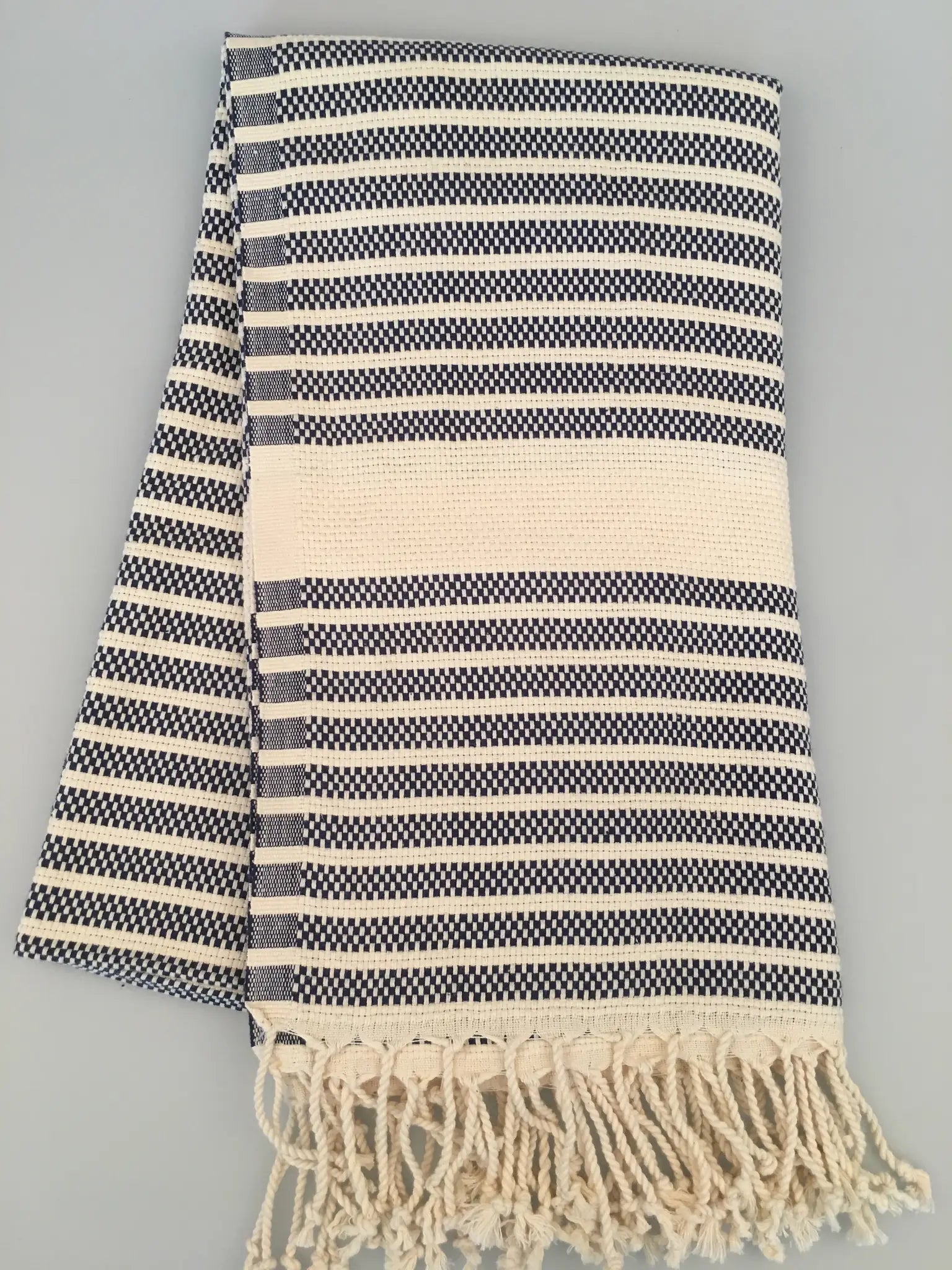 "Navy and white striped Hittite Turkish towel with fringed edges, laid flat on a light background."