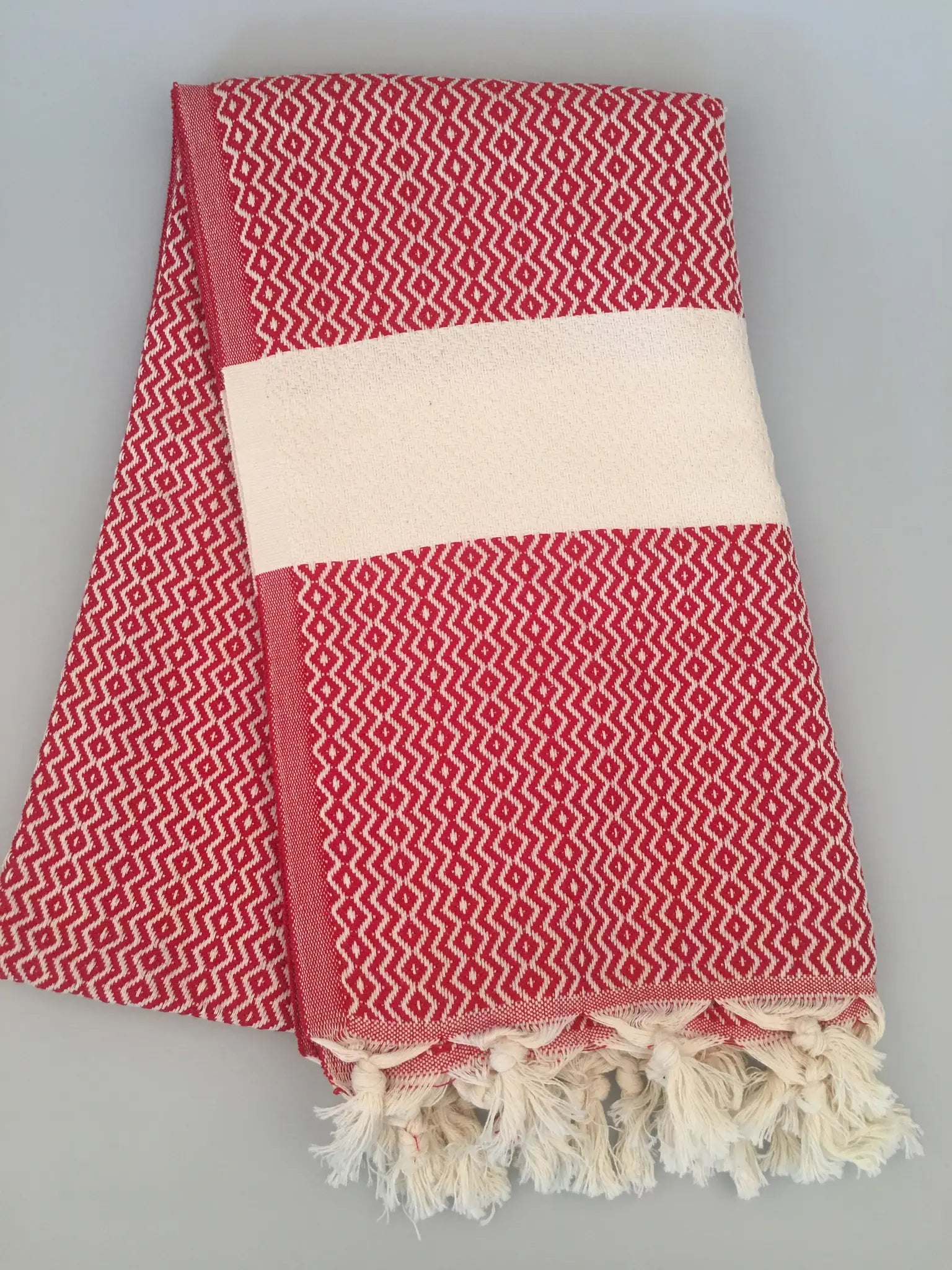 Red and white patterned Turkish towel with fringed edges, folded neatly, showcasing a textured design.