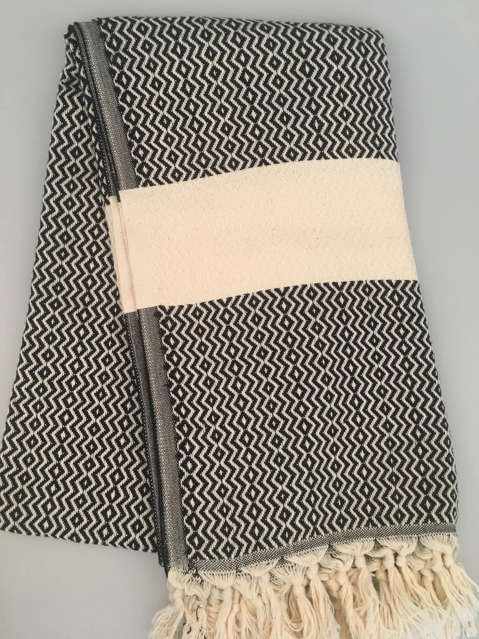 "Black and white patterned Turkish towel with cream stripe and fringed edges, folded neatly."