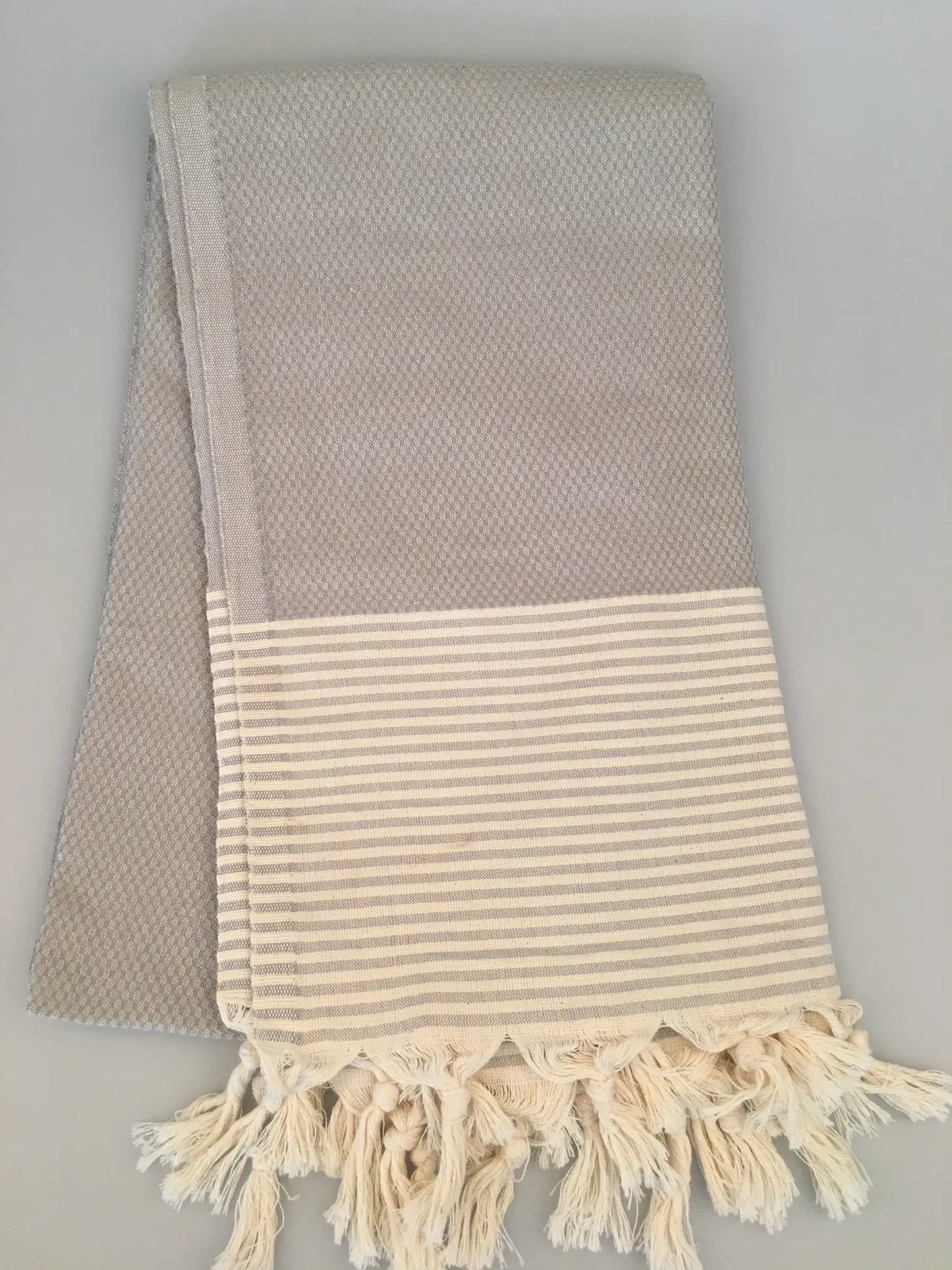 "Gray Miletus Turkish towel peshtemal with a textured pattern and cream-striped hem, fringed edges."