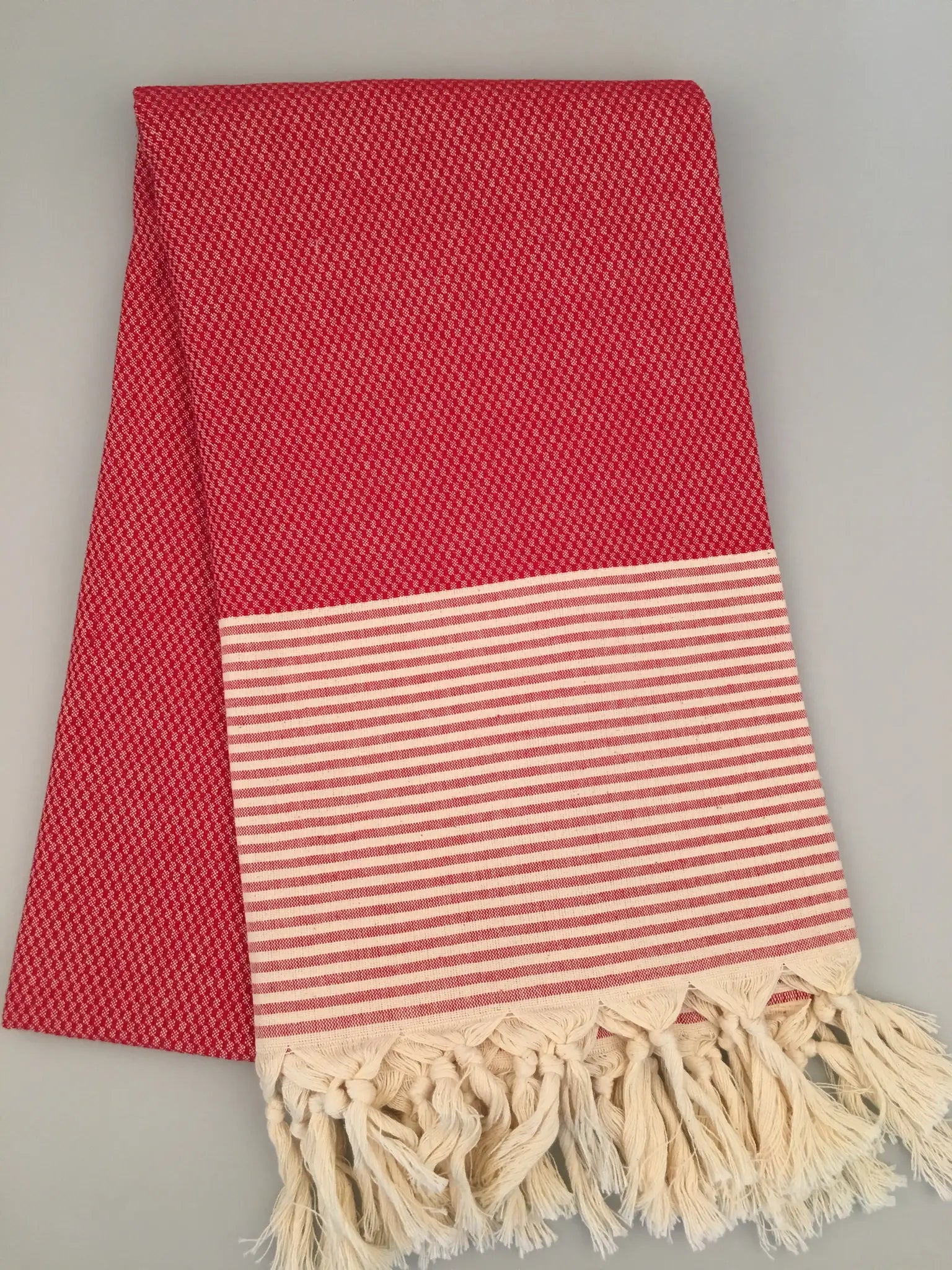 Red Turkish towel with textured pattern, featuring a striped white and red border and fringed edges, laid flat.