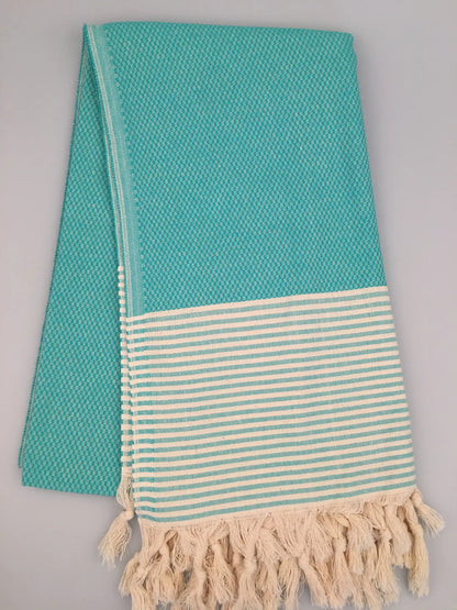 Turquoise Turkish towel with a textured weave, featuring a striped cream and turquoise border and fringed ends.