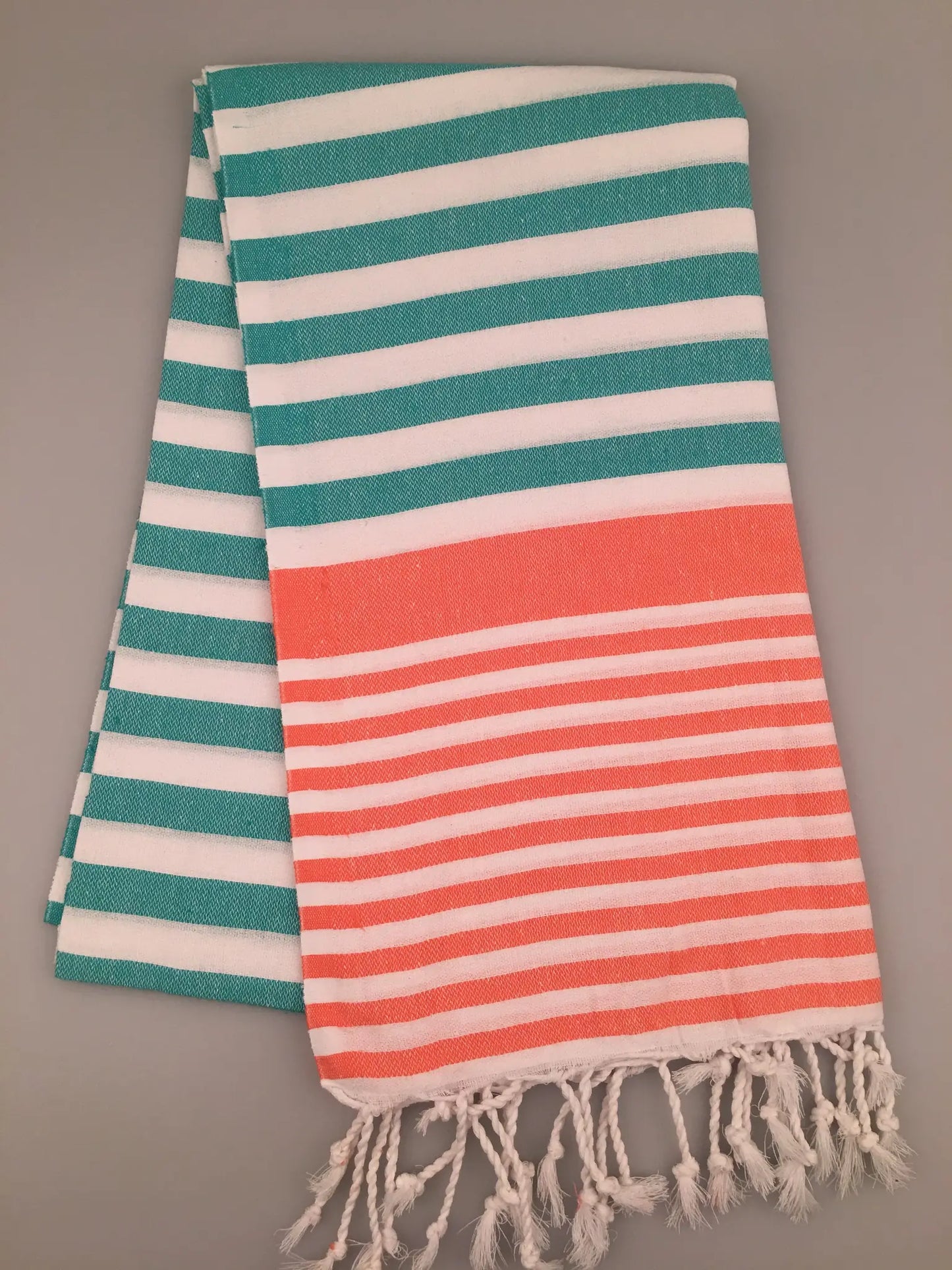 "Striped Turkish towel in turquoise and white with an orange band, featuring fringed ends, folded view."