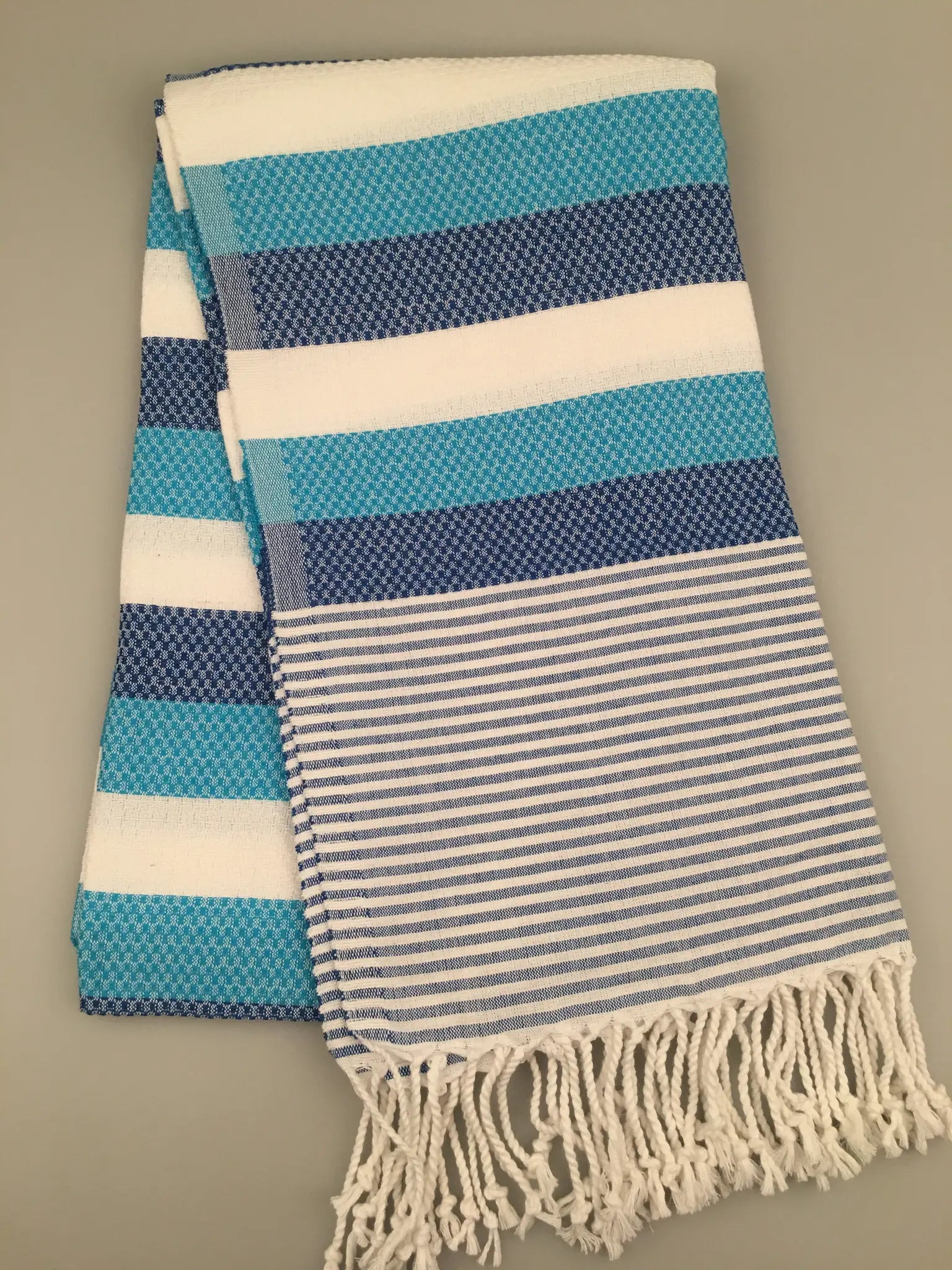 Turquoise and white striped Turkish towel with fringed edges, folded neatly.