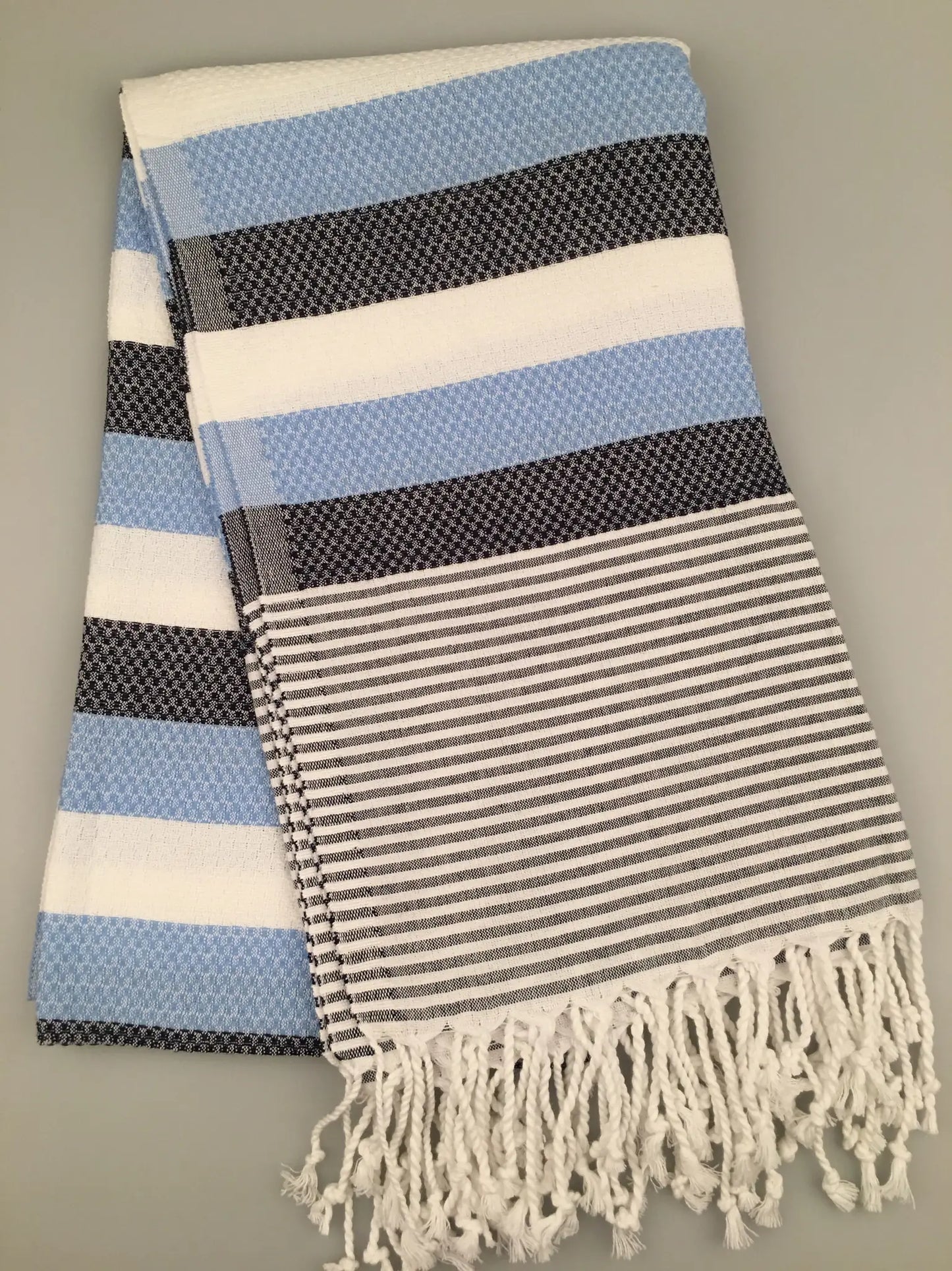 "Blue and white striped Turkish towel with textured patterns and fringed edges, folded view"