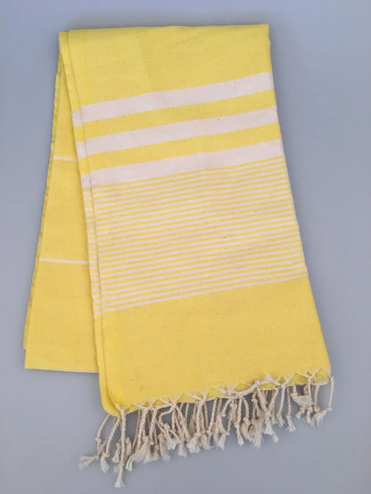 "Yellow Turkish towel peshtemal with white stripes and fringed edges, laid flat on a light gray background."