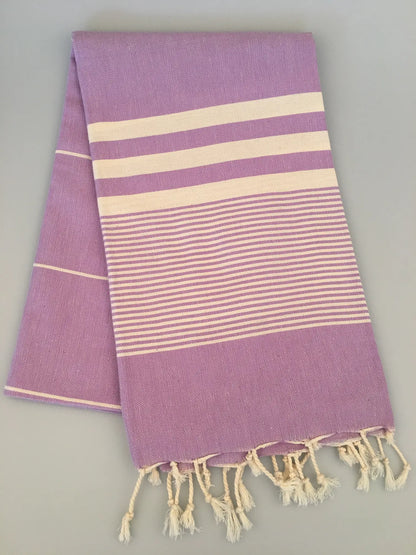 Lavender Turkish towel peshtemal with cream stripes and fringed edges, laid flat on a light background.