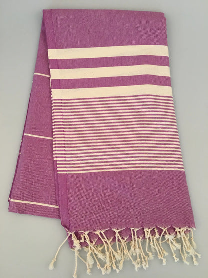 "Purple Turkish towel peshtemal with cream stripes and fringed edges, folded flat on a light background."