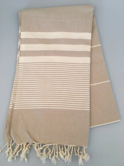 Beige Turkish towel with white striped pattern and fringed edges, folded neatly on a gray background.
