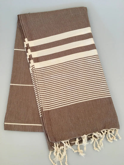 "Brown and cream striped Turkish towel with fringe edges, folded neatly on a light gray surface."