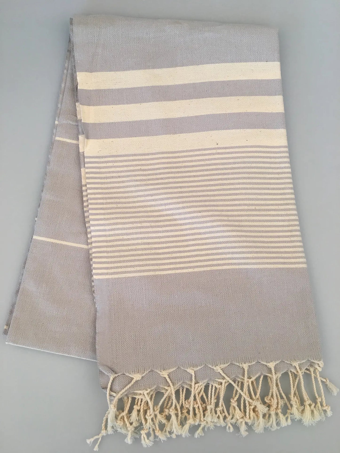 "Light gray Turkish towel with white stripes and fringed edges, folded view on a gray background."