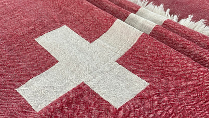 Red fabric with a white cross pattern, textured weave, and fringed edges, close-up view.